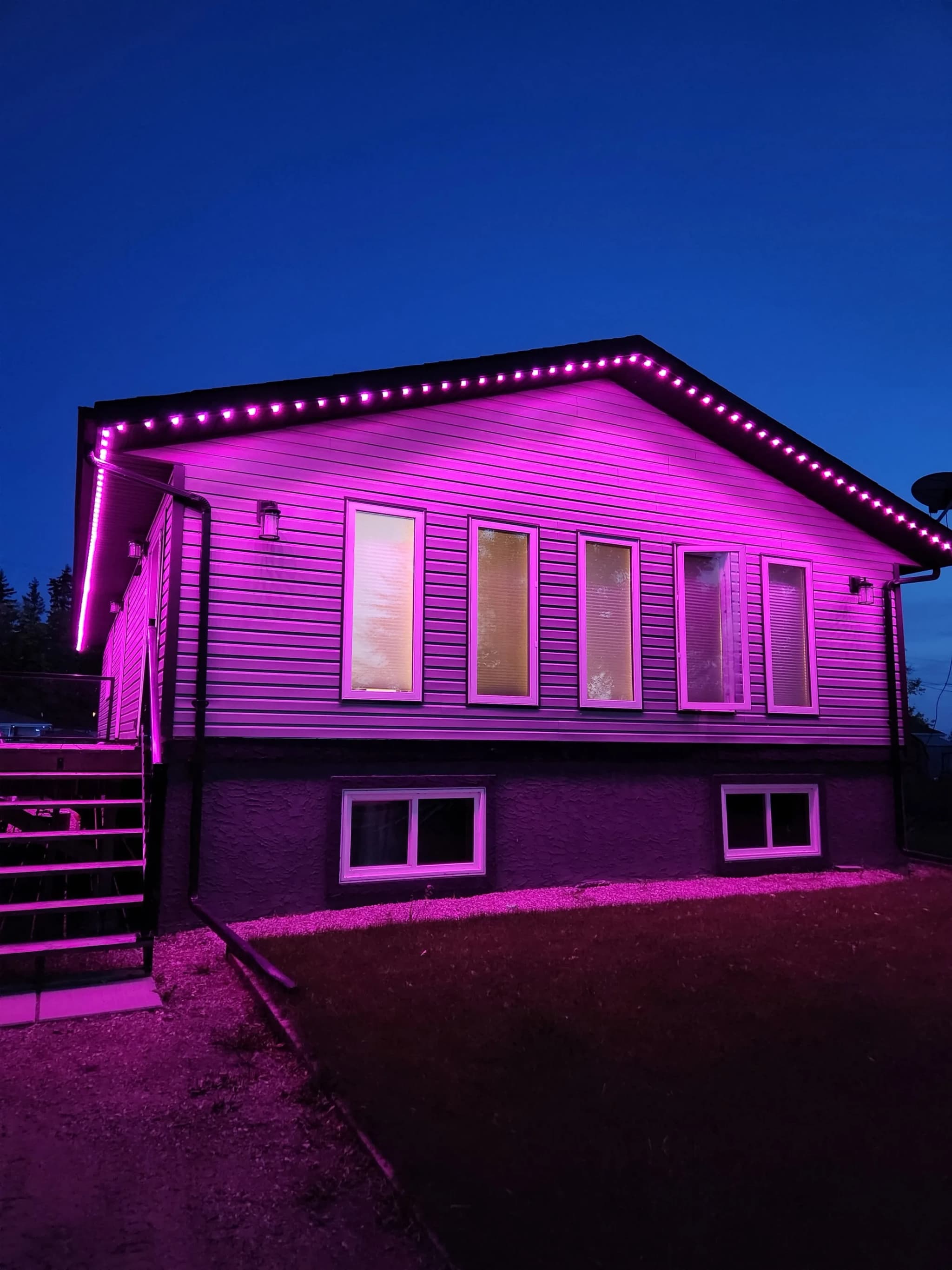Track-mounted RGBW LED lights washing a house facade in pink and magenta