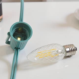 Warm white faceted C9 bulb beside a green E17 socket